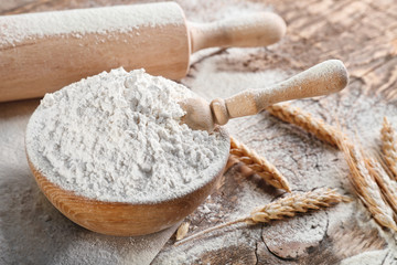 Bowl of flour and scoop on wooden background