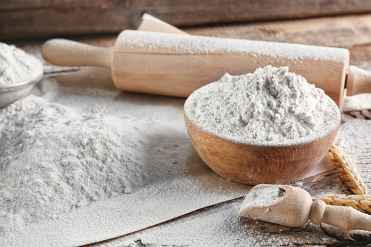 Bowl of flour and rolling pin on wooden background