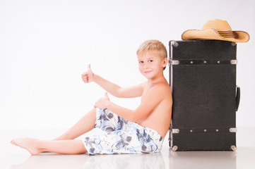 Little boy traveler in hat sits on suitcase