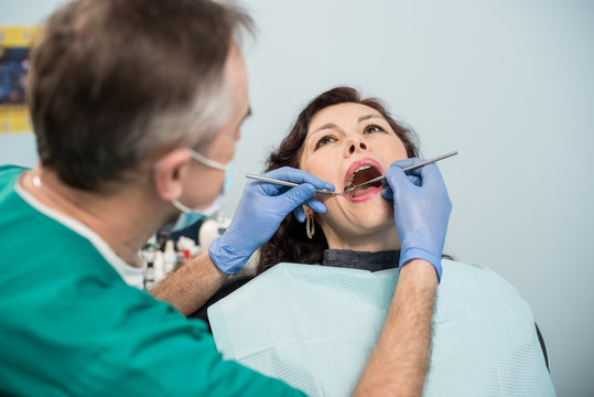 Woman having dental check up in dental office. Dentist examining a patient's teeth with dental tools - mirror and probe. Dentistry.