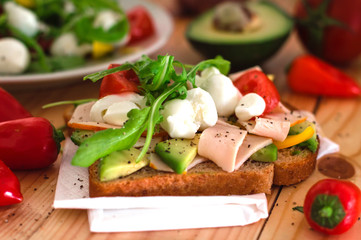 Toast with avocado, arugula, ham and mozzarella. Wooden background. Close-up. Top view