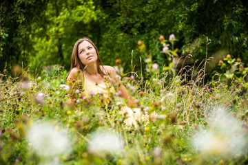 Beautiful woman enjoys nature in summer bloom. Lonely girl has a beautiful face. The woman sits in the meadow. Blurry background.