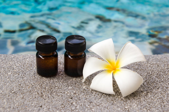 Two bottles of aroma essential oil and flower of frangipani on the swimming pool background for spa theme.