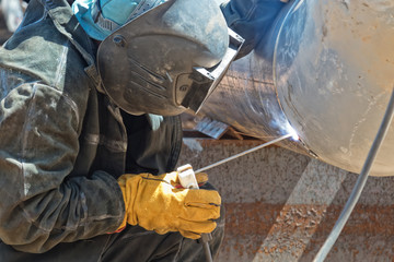 A welder in protective clothing performs the welding of the n element of the process pipeline