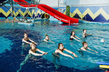 Fitness group of girls doing aerobical excercises in swimming pool at aqua park. Sport and leisure...