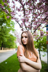 Naklejka premium Outdoor portrait of young beautiful fashionable lady posing near flowering tree sakura