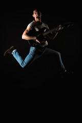 Music and creativity. Handsome young man in a T-shirt and jeans, jumping with an electric guitar, on a black isolated background. Vertical frame