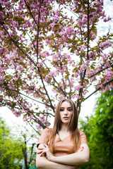 Naklejka premium Outdoor portrait of young beautiful happy smiling lady posing near flowering tree sakura