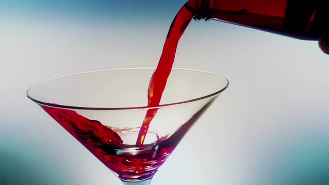 pouring red fresh alcohol cocktail drink glass with ice cubes on blue light tint background, shot slow motion, fun and dance disco concept