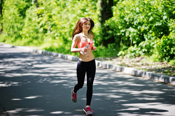 Fitness sport girl in sportswear run at road in forest with bottle water on hand, outdoor sports, urban style.