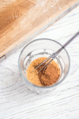 Mixing brown sugar and cinnamon in a glass. Baking ingredients on white wooden table.