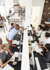 Man passing document in busy open plan office, vertical