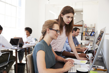 Two women working together at computer in open plan office