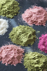 Various colorful superfood powders on dark background. Healthy food supplements, detoxing concept
