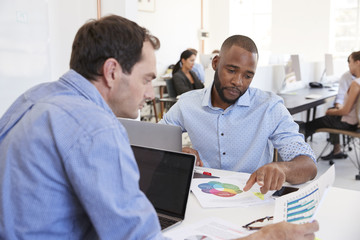 Two men discussing documents in a busy office