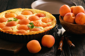 Homemade cheesecake with apricots on black wooden background.