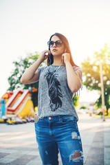 Urban vintage portrait of beautiful and attractive girl with sunglasses and headphones. She walks and listens to music. Warm summer colors and haze. Strong back light.