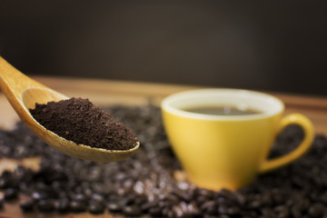 Roasted coffee on wooden spoon with coffee beans and yellow mug blurred background.