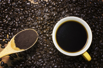 Hot Black Coffee in mug and coffee beans roasted with wooden spoon on wooden table.