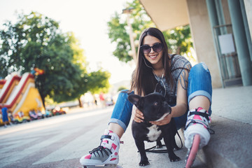 Warm summer colors and haze. Strong back light. Roller skates girl with sitting on city square with her French bulldog and enjoying hot afternoon.