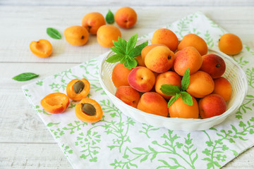 Ripe apricots in a basket on a light wooden background.