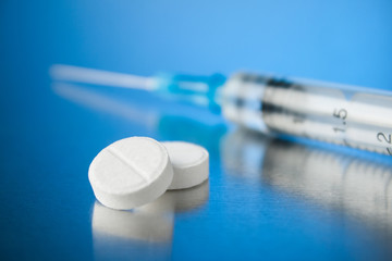 Fototapeta na wymiar White pills with a syringe on a blue background.