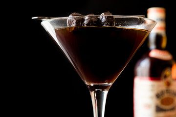Black Manhattan Cocktail with olives on dark wooden surface.