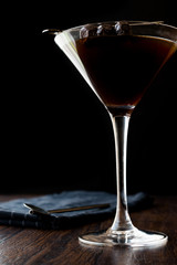 Black Manhattan Cocktail with olives on dark wooden surface.