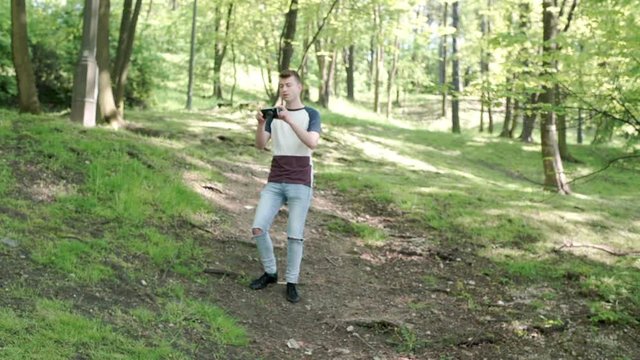 Man walking on pathway in the forest and doing photos on old camera, steadycam shot

