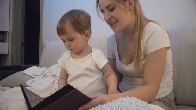 Mother with baby son looking through family photo album in bed at night