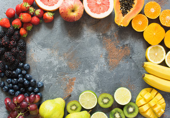 DIfferent rainbow colored fruits and berries arranged in a circle, on the grey stone background, copy space for text, selective focus