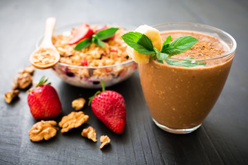Oatmeal porridge with blueberries, strawberries, muesli and chocolate banana smoothie on wooden table. Morning breakfast.