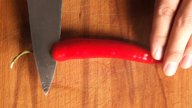 cutting red hot pepper on cutting board. professional chef's hand using knife to slice, chop chilli pepper for cooking. chili pepper being diced on wooden board top view. Healthy food. Close-up
