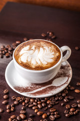 white cup of cappuccino on an old wooden table, coffee beans scattered on the table