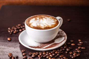 white cup of cappuccino on an old wooden table, coffee beans scattered on the table