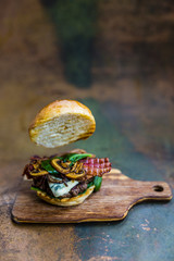 Tasty grilled beef burger with spinach lettuce and blue cheese served on rusty table with copyspace, blackboard in background.