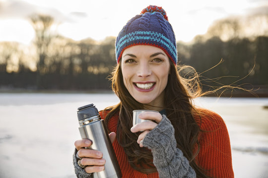 Portrait of smiling woman drinking hot beverage from thermos flask outdoors in winter