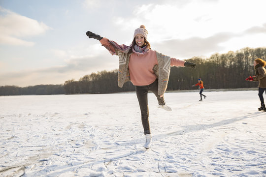 Woman dancing with ice skates on frozen lake with friends
