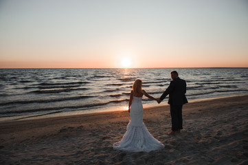 young couple stands at the sea beach looking at sunset