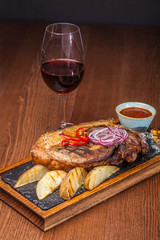 big fat fried steak on a wooden board with onions and fried potatoes with Bachall red wine, a nice feed at restaurant