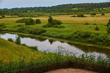 River view/Summer, noon. Under the hill below there is a small river. Growing trees. Trees create a shadow. In the distance you can see the forest. Russia, Pskov region, landscape, nature