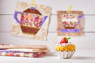 The pin cushion like a cupcake with strawberry and patchwork blocks of the cup and the teapot with a pattern of flowers hanging on wall