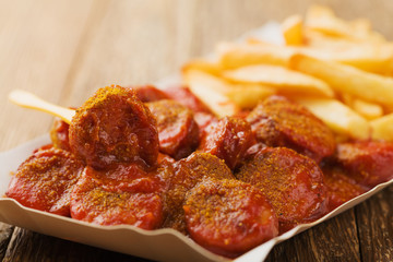 Traditional German currywurst, served with chips on disposable paper tray.