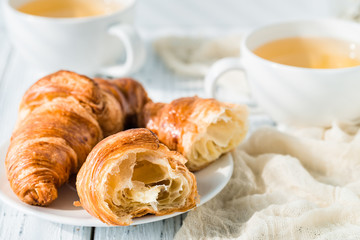 Croissants with cups of herbal tea on white rustic table