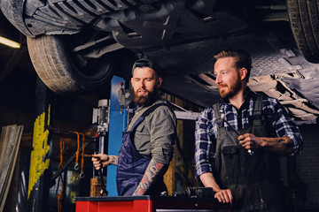 Obraz na płótnie Canvas Two mechanics working under the car in a garage.