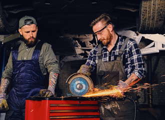 Fototapeta na wymiar Two b mechanics working with an angle grinder in a garage.