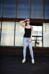 Fototapeta na wymiar Girl at sunglasses and jeans posed at the roof of abadoned industrial place with windows.