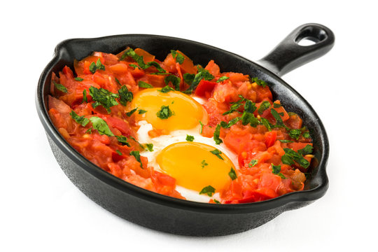 Shakshuka in iron frying pan isolated on white background. Typical food in Israel.

