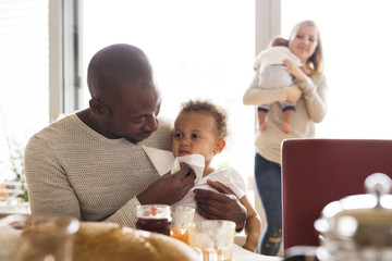 Young interracial family with little children having breakfast.