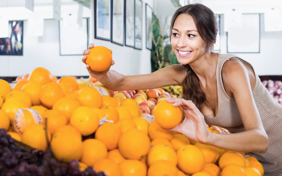 Young cheerful woman customer choosing ripe oranges